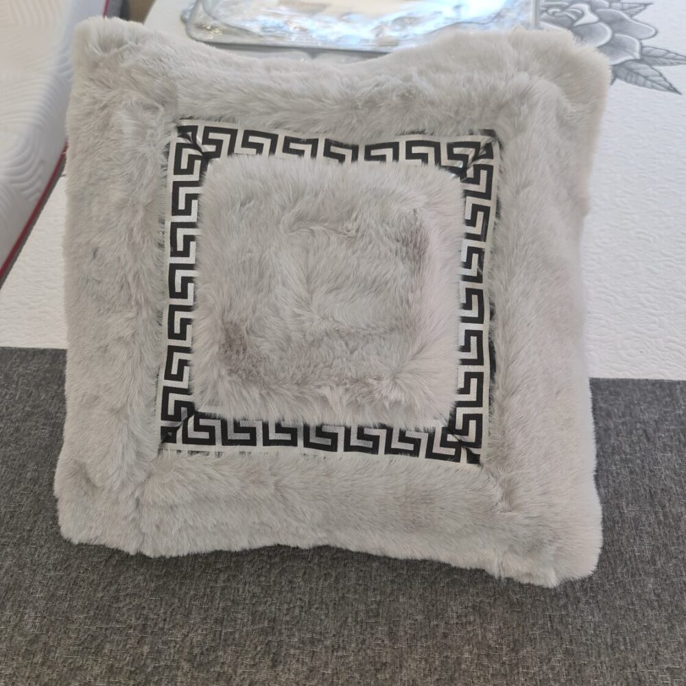 Cojín decorativo de piel sintética gris presenta un diseño de greca griega negra en el centro y una textura suave y esponjosa